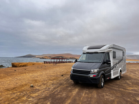 Modern RV motorhome while standing desert landscape  next to red sand beach in National Park Reserve Paracas in Pisco Province, Peru. Caravan exploring red sand beaches, and wildlife of national park.