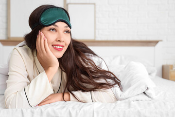 Beautiful young woman with sleep mask lying in bed at home