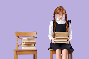 Shocked redhead schoolgirl with stack of books sitting in chair on lilac background