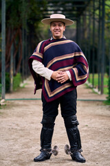 Portrait of a smiling, cheerful young man dressed as a Chilean huaso, celebrating and posing to...
