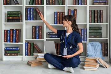 Female medical intern studying with laptop in library