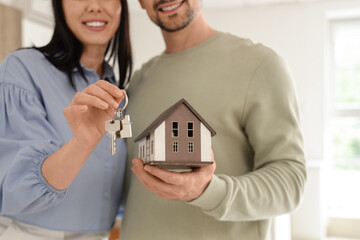 Happy young couple with house model and key from their new flat in kitchen, closeup