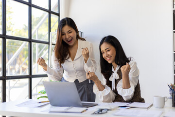 Employees and female co-workers are excited and happy about their promotions and bonuses while looking at their laptop.