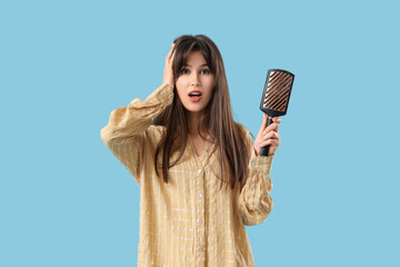 Worried young woman with hair loss problem and brush on blue background
