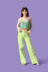 Stylish young woman in green pants on lilac background