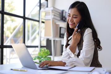 A serious female employee is busy with paperwork and talking on the phone with the boss.
