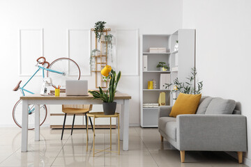 Interior of light home office with workplace, bicycle and sofa