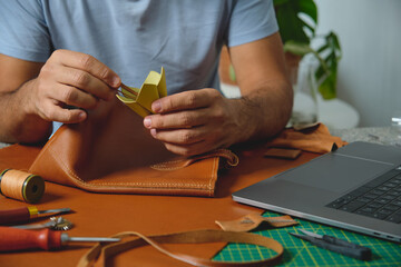 Leather craftsman gluing lining to brown leather bag in workshop
