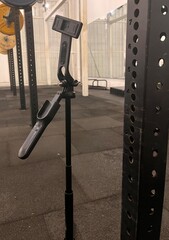 Close-up of a black steel squat rack in a modern gym setting. Featuring adjustable J-hooks and...