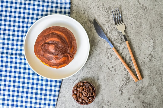 Top view of coffee bun on plate with napkin. grey or gray cement as background. High angle, above, close up. blue, white. bread home made. fork, knife. roasted coffee beans, little pottery or earthern