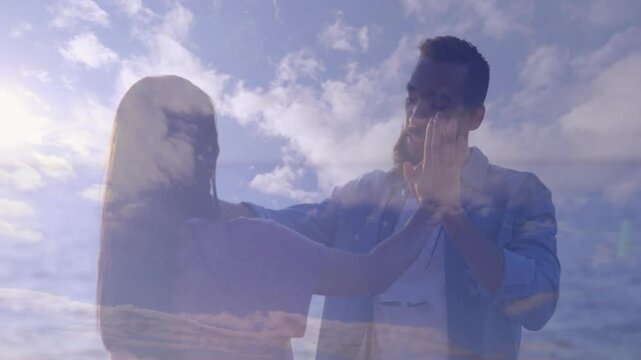 Couple lifting hands on shore, initiating hand slap rhythm, showing cloud overlay for technology ad