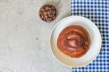Top view of coffee bun on plate with napkin. grey or gray cement as background. High angle, above. blue, white. copy space, free, empty, negative. bread home made. coffee beans.
