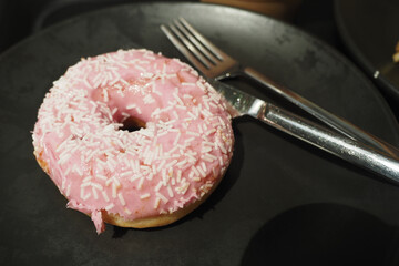 Pink frosted donut with sprinkles on a dark plate