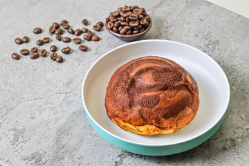 Close up view of coffee bun on plate with napkin. grey or gray cement as background. blue, white. bread home made. roasted coffee beans, little pottery or earthern.