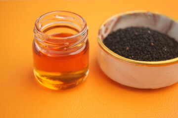 Black seeds and amber oil are presented on a vibrant orange surface