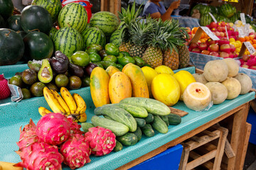 Tropical fruits including watermelon, pineapple, papaya, dragon fruit, and cucumbers at market...