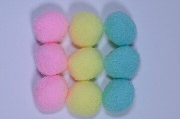 Grid of pastel pompom balls in pink yellow and teal arranged on white background