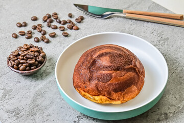 Close up view of coffee bun on plate with fork, knife and roasted coffee beans isolated on grey or gray cement as background. bread home made.