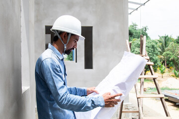 Asian or Indian engineering man wearing white helmet hard hat at construction site before working...