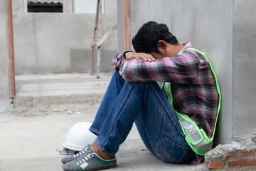 Hopeless builder worker sitting in construction site bend head down in his knee, stressed Asian...