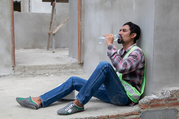 Hopeless builder worker sitting in construction site bend head down in his knee, stressed Asian...