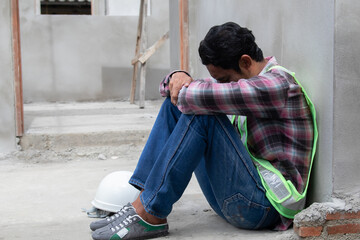 Hopeless builder worker sitting in construction site bend head down in his knee, stressed Asian...