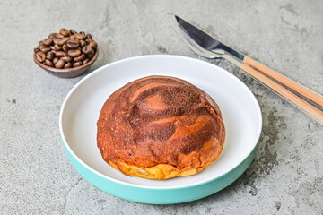 Close up view of coffee bun on plate with fork, knife and roasted coffee beans isolated on grey or gray cement as background. bread home made.