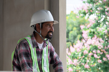 Asian laborers man wearing safety reflected vests sitting at townhouse construction site or resort talking to a contractor using mobile phone, foreman relaxing communication with colleagues