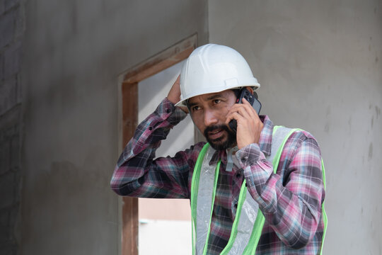 Asian laborers man wearing safety reflected vests sitting at townhouse construction site or resort talking to a contractor using mobile phone, foreman relaxing communication with colleagues