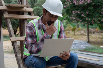 Thoughtful Indian contractor with mustache construction small business owner using laptop...