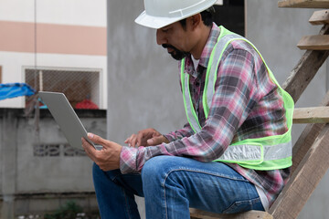 Thoughtful Indian contractor with mustache construction small business owner using laptop...