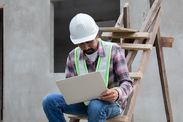 Thoughtful Indian contractor with mustache construction small business owner using laptop...