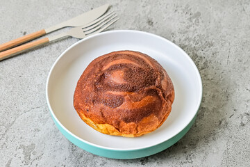 Close up view of coffee bun on plate with fork and knife isoalted on grey or gray cement as background. bread home made. copy space, empty, free, negative, text.