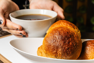 horizontal close-up photo of traditional whole grain artisan mogolla breads with woman's hands holding cup of coffee in healthy vegetarian restaurant in Colombia.