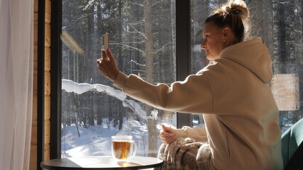 Woman takes selfie near winter window enjoying solitude yet sharing moment through selfie Cozy...