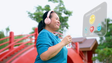 Content senior Asian woman with headphones drinking water, checking hydration and heart rate on a...