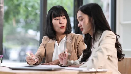 Two young businesswoman are actively discussing a project, reviewing document, and sharing ideas in a contemporary office, demonstrating teamwork and collaboration.