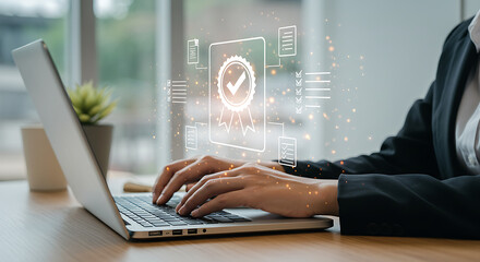 Fototapeta premium Person typing on laptop with quality assurance graphic overlayed on the screen display in bright light