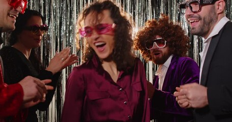 Cheerful group of friends dancing and celebrating at retro themed party with sparkling decorations. Smiling people wearing colorful outfits and funky glasses, enjoying joyful nightlife atmosphere.