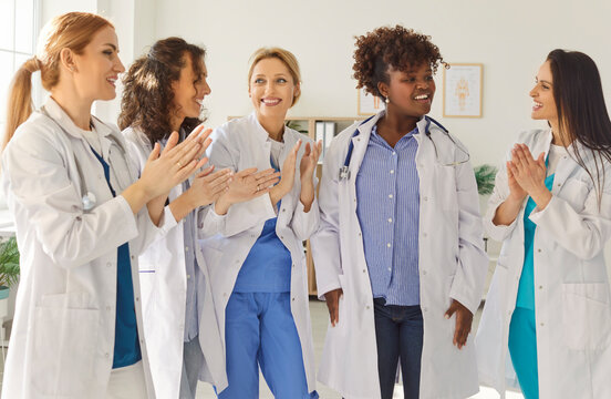 Medicine concept. Group of medical workers wearing white coats meet new colleague in their team, clapping hands and introducing themselves. Nurses or doctors meeting together in clinic - Powered by Adobe