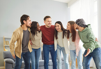 Fototapeta premium Cheerful friend group meeting, multiethnic team of young people giving common hug, enjoying kind and pleasant teamwork, celebrating unity success, achievement, win, successful cooperation, joy at home