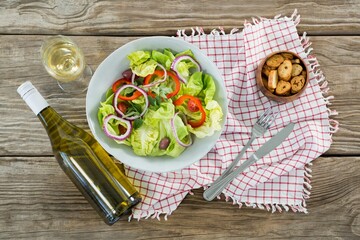 Fresh salad in bowl by wine bottle on wooden table