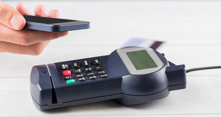 Flat design POS terminal is resting on light wood surface with card inserted and smartphone tapping