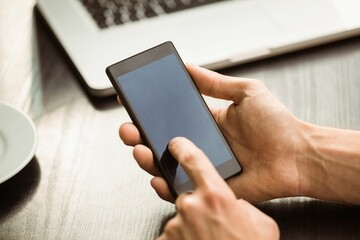 Smartphone is being tapped in flat design on wooden tabletop with laptop and cup, copy space