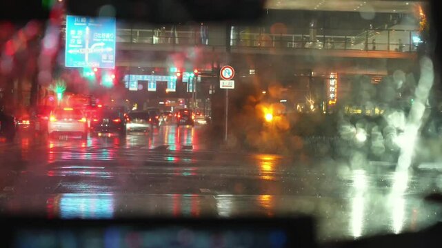 Through the rain-blurred car window, see rainy night street. Neon lights reflect off the traffic, and hazy moisture creates a dreamy, colorful scene.