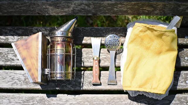 Beekeeper tools (smoker, hive tools, suit) on weathered wooden bench