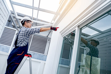 Asian man construction worker climbing up on an aluminium ladder pointing at window frame of a new...