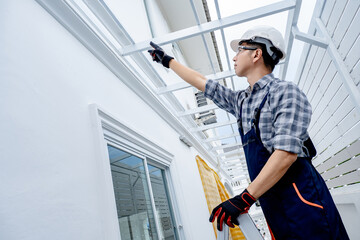 Asian male foreman or construction worker climbing up on an aluminium ladder pointing at the roof...