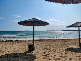 Beach, straw umbrellas, sea, empty sky and island in the distance