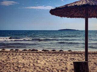 Beach, straw umbrellas, sea, empty sky and island in the distance